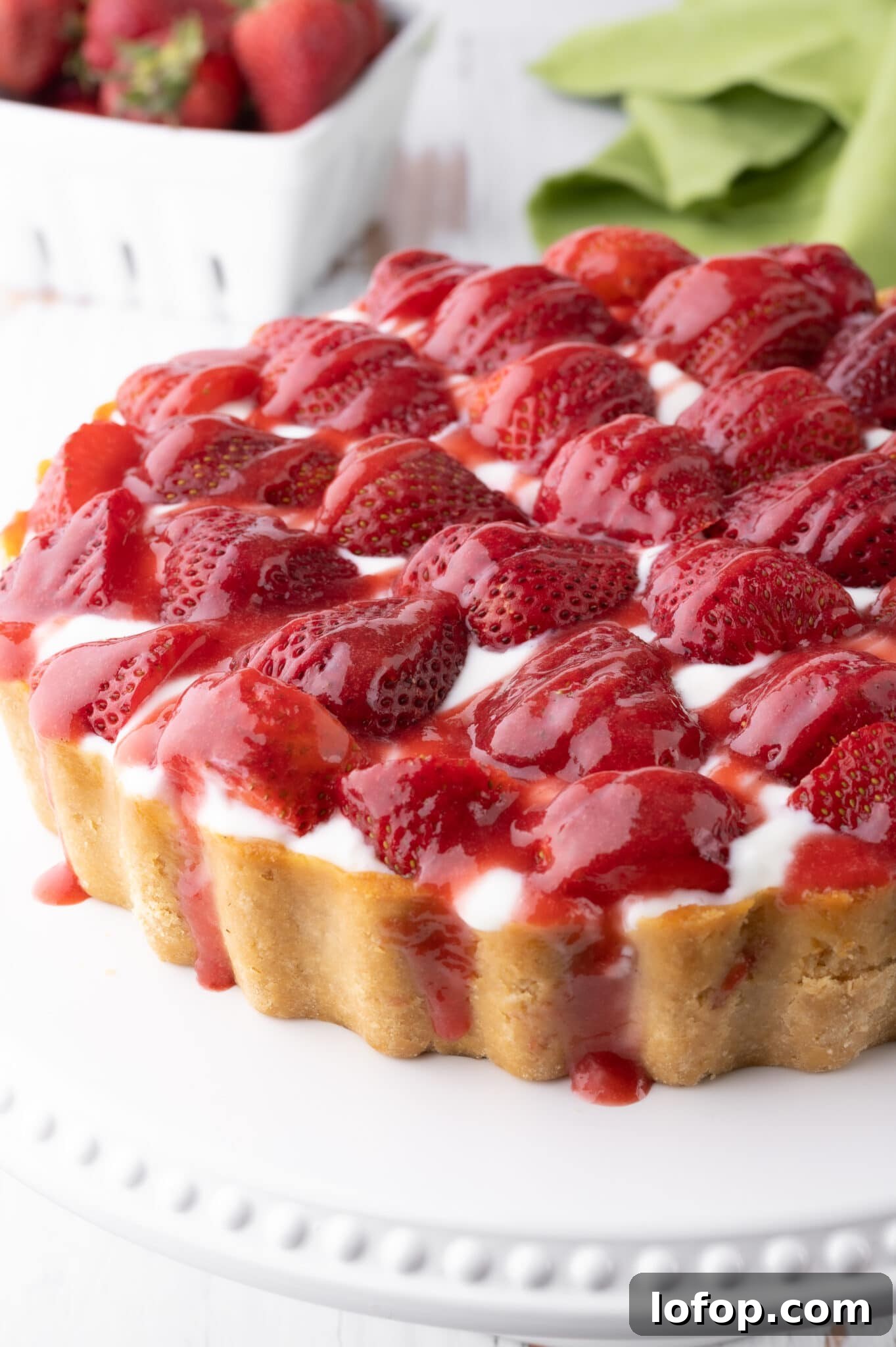 Keto strawberry cheesecake with fresh strawberries and drizzled with strawberry sauce.  The cheesecake rests on a bright white cake stand. 