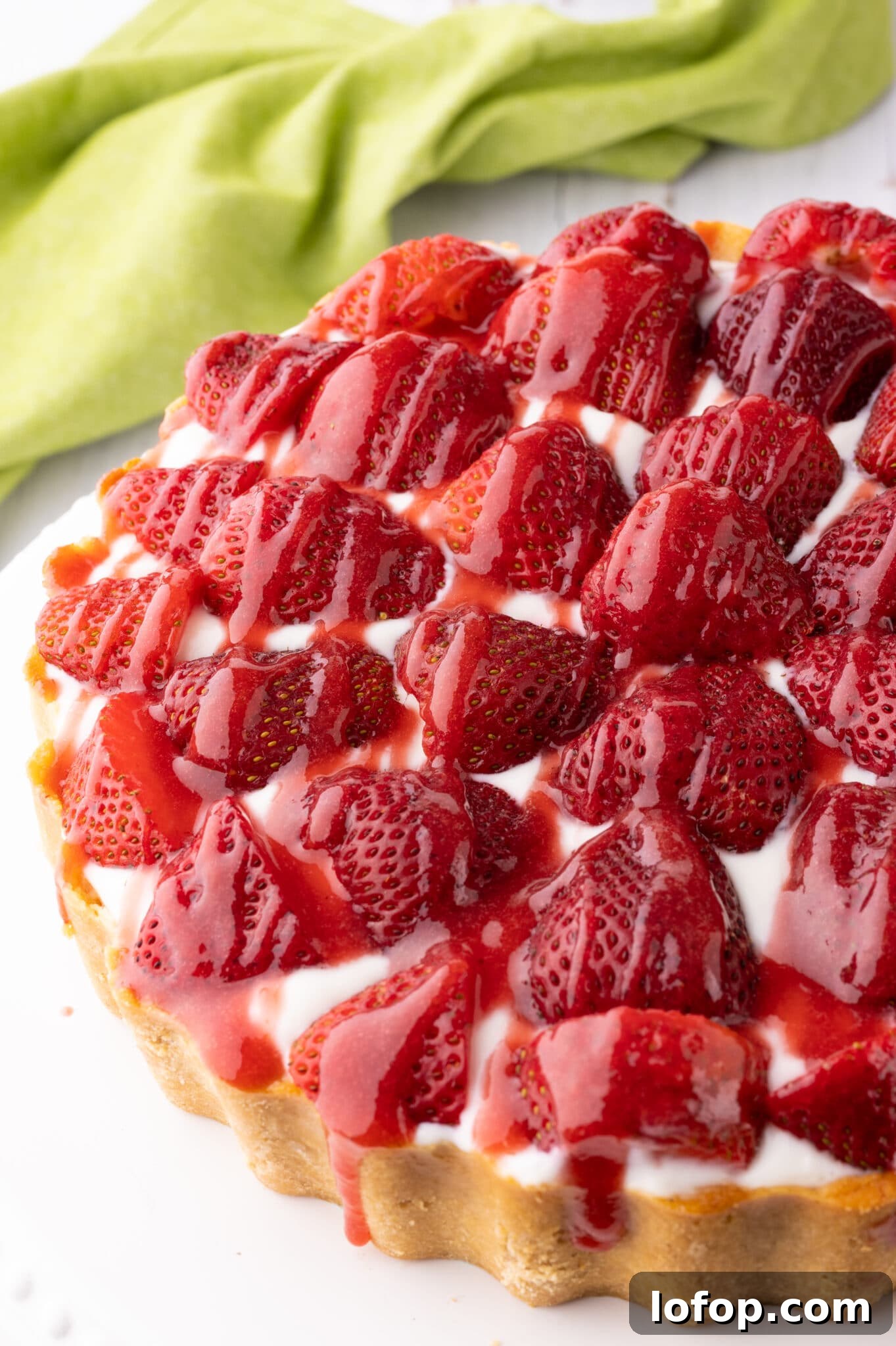 Keto strawberry cheesecake with fresh strawberries and drizzled with strawberry sauce.  The cheesecake rests on a bright white cake stand. 
