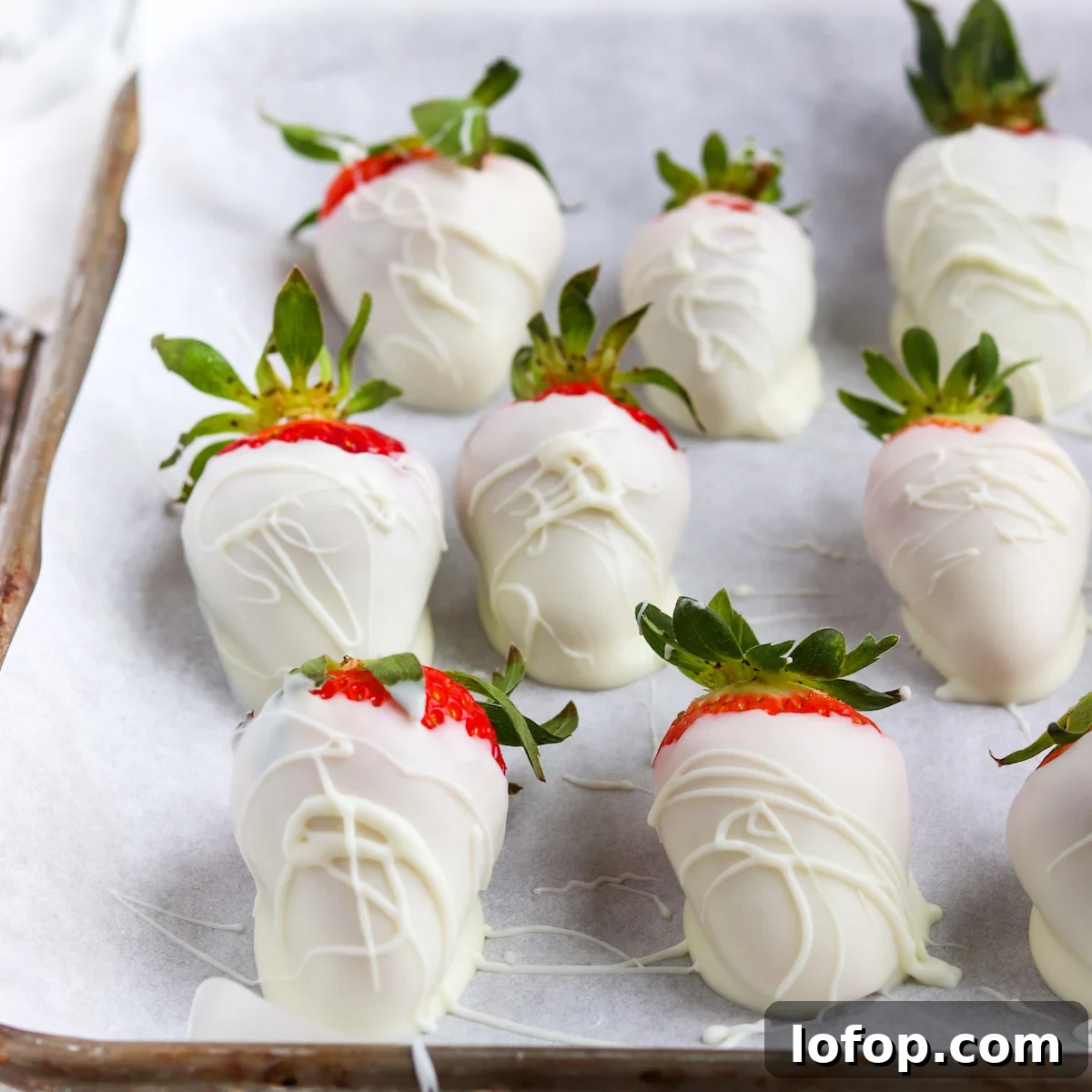 closeup of strawberries dipped in white chocolate on a parchment lined baking sheet.