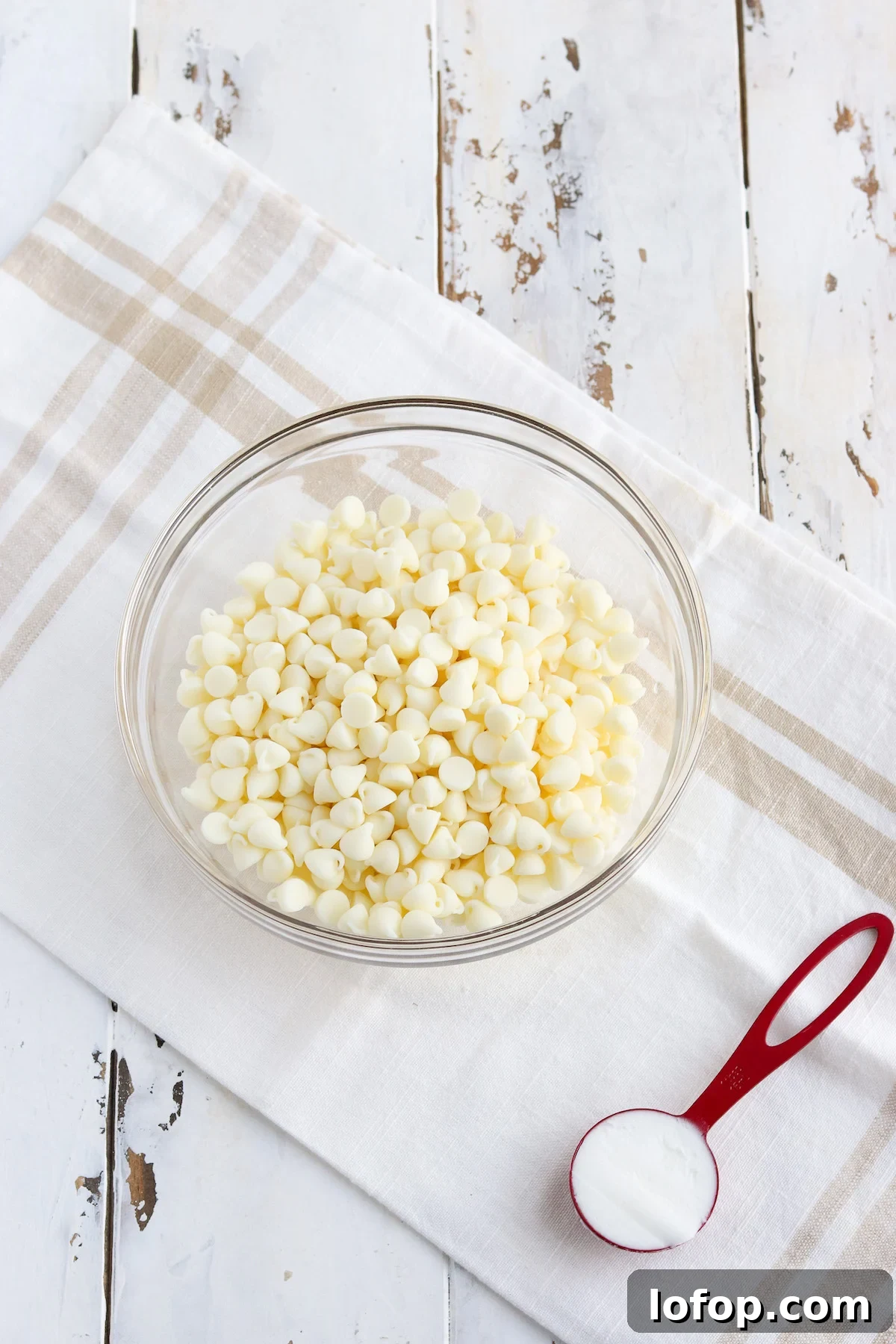 Glass bowl of high quality white chocolate chips and one tablespoon of shortening preparing to melt.