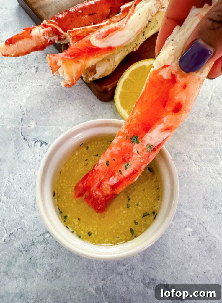 Garlic Butter Grilled King Crab Legs Recipe 10 person holding cracked king crab leg in melted butter