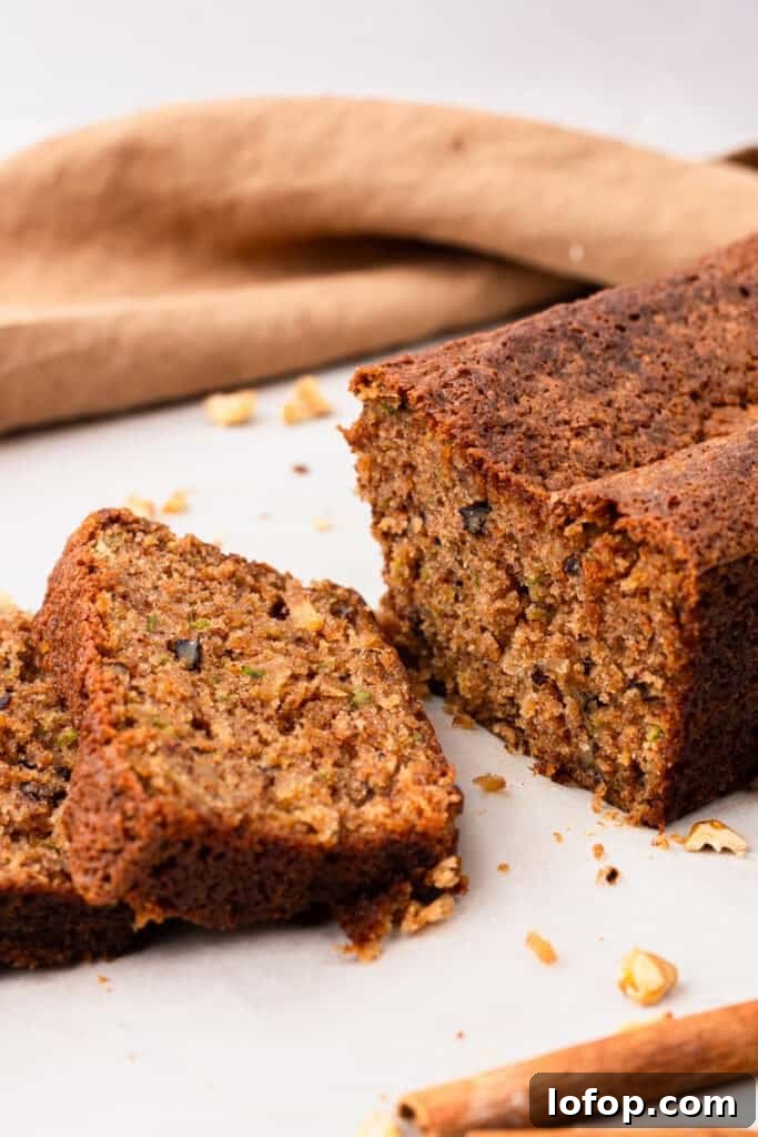 Ultra-Moist Gluten-Free Zucchini Bread with a Secret Ingredient 7 side view of Extra Moist Gluten Free Zucchini Bread on a plate with two slices cut out of the bread with crumbs on the plate