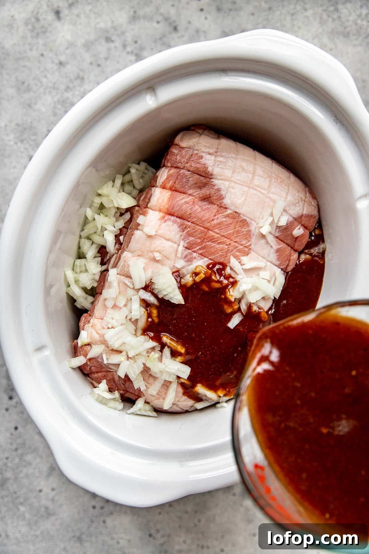 Sauce being poured onto pulled pork in a white slow cooker.