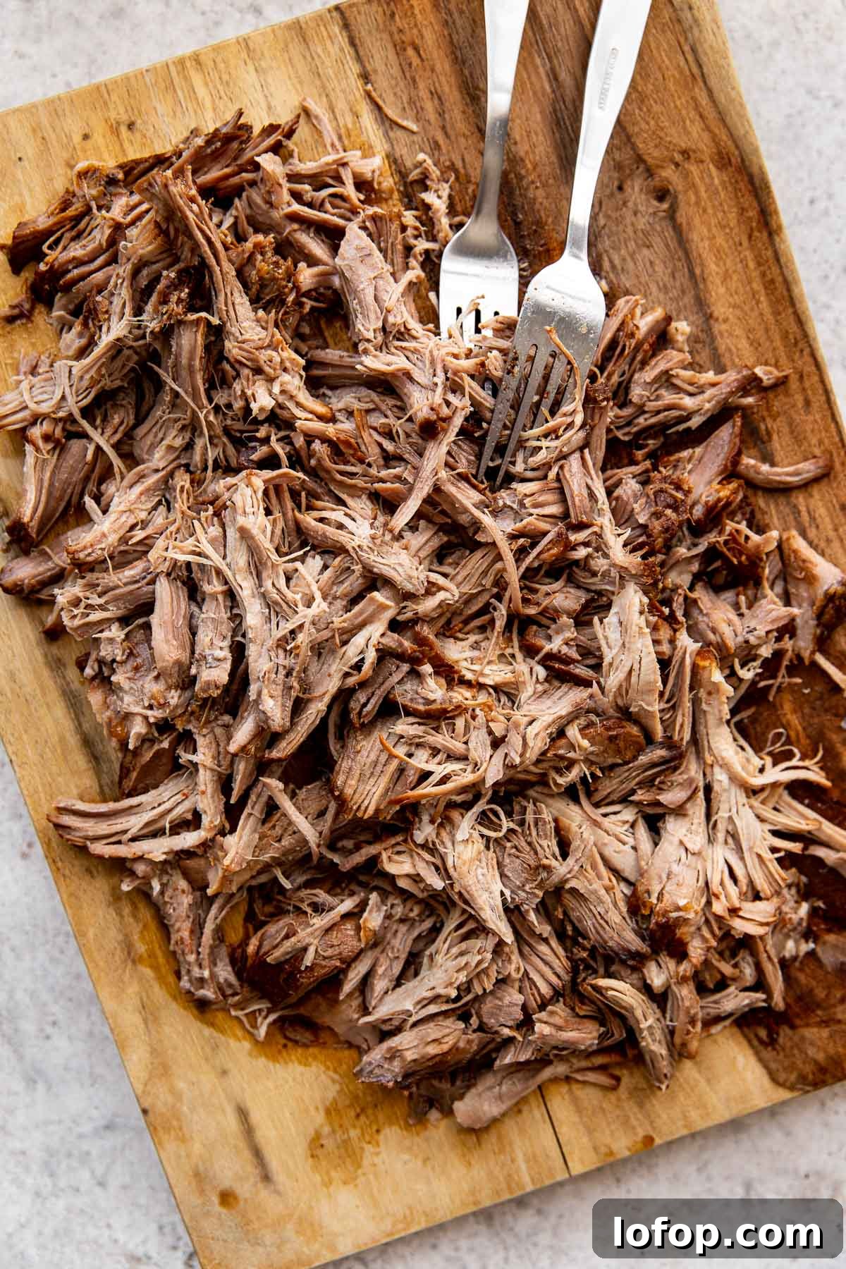 pulled pork shredded with forks on a cutting board.