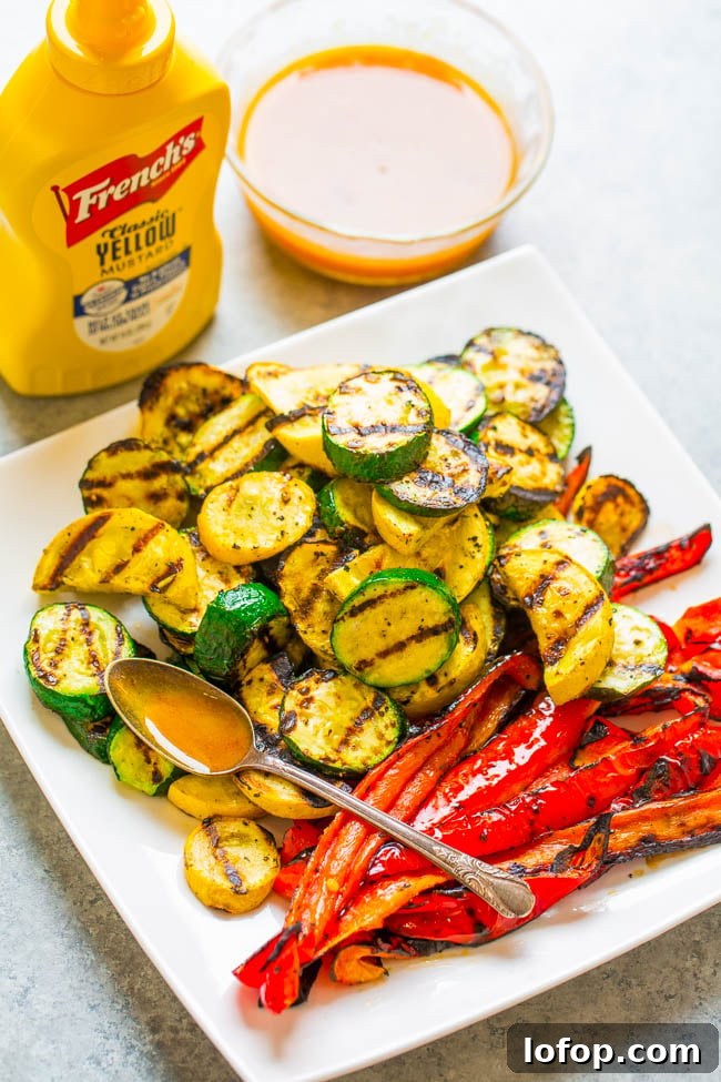 A plate of grilled zucchini and red bell peppers with a spoon, served alongside a bowl of sauce and a bottle of French’s yellow mustard.