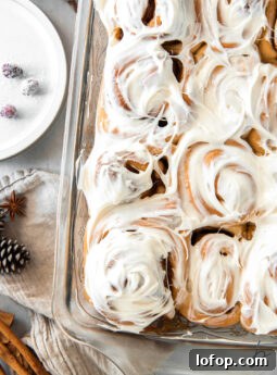pan of gingerbread cinnamon rolls topped with cream cheese frosting.