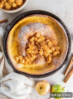 apple dutch baby in a skillet with hand wrapped with kitchen towel.