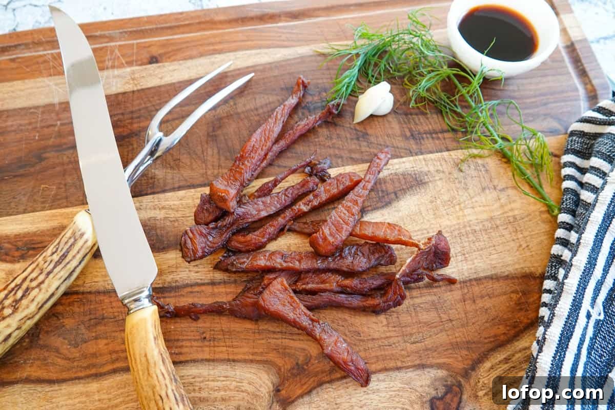 Homemade Turkey Jerky Recipe: Tender, Flavorful & Easy to Make 12 Turkey jerky on cutting board with carving knife and dish of soy sauce