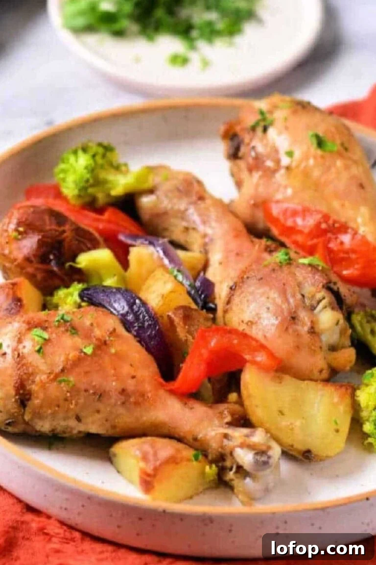 A sheet pan with roasted chicken drumsticks, potatoes, and mixed vegetables, including broccoli and bell peppers.