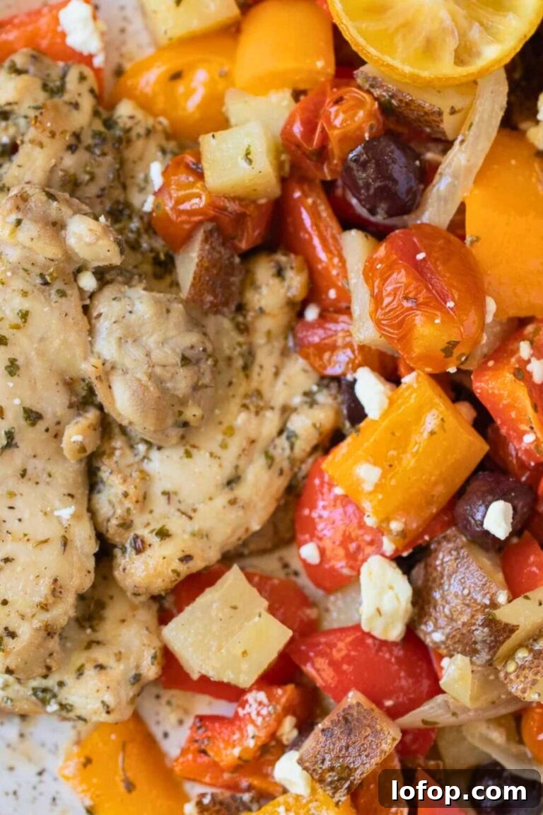 A sheet pan filled with roasted chicken pieces, sausage, potatoes, and assorted vegetables like carrots and bell peppers, garnished with fresh herbs.