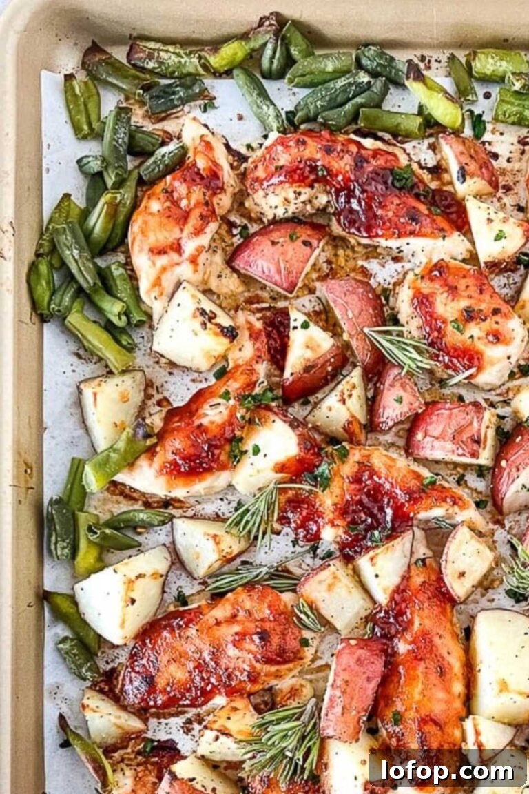 Glazed chicken breasts with roasted red potatoes and green beans, seasoned with rosemary sprigs on a baking sheet.