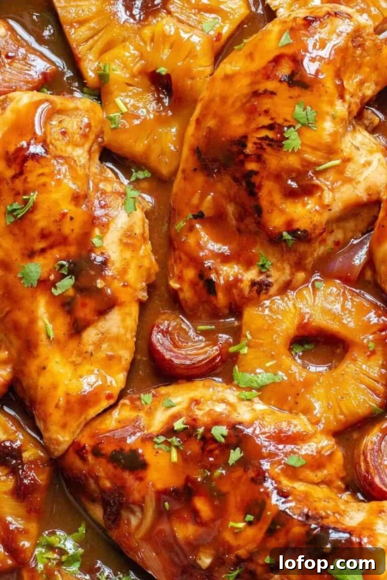 A sheet pan filled with glazed barbecue chicken breasts and pineapple slices, garnished with parsley.
