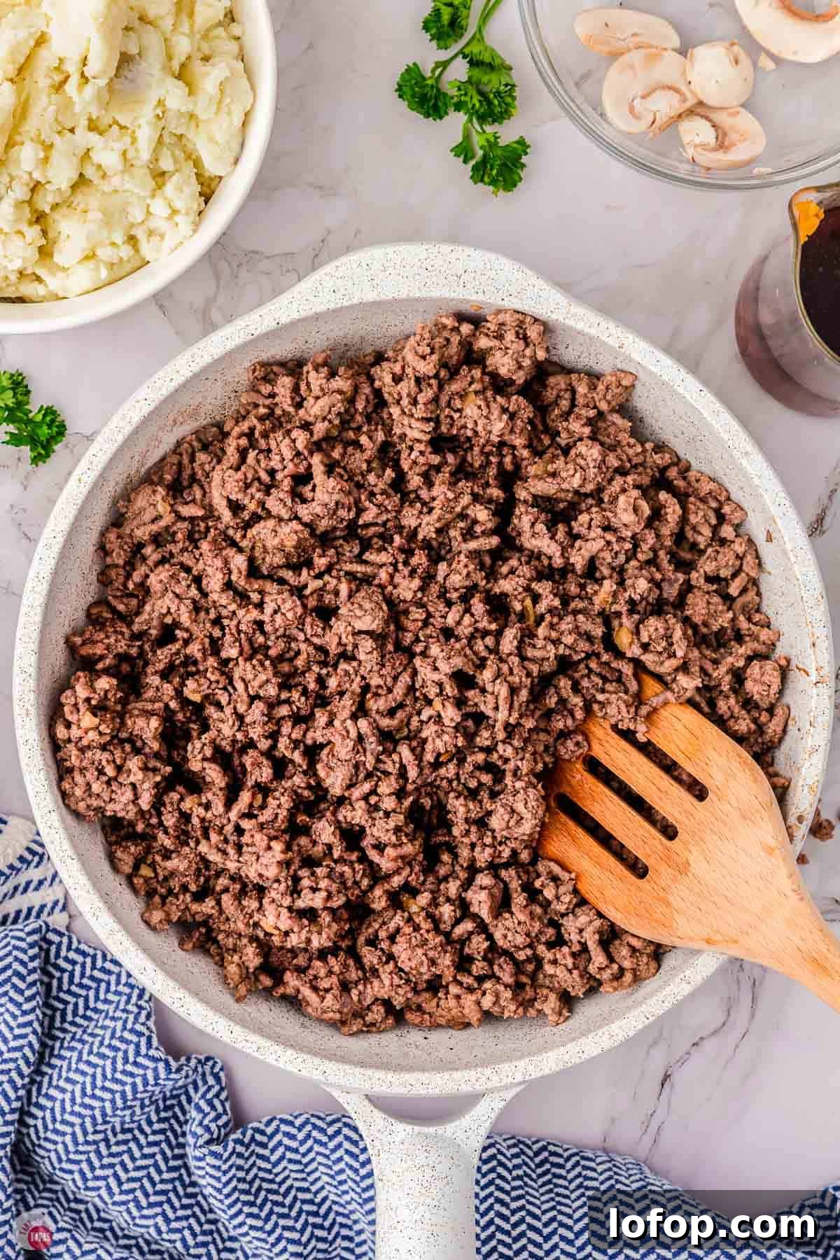 Hearty Salisbury Steak Casserole with Savory Brown Gravy 5 cooked ground beef in a white skillet with a wood spoon