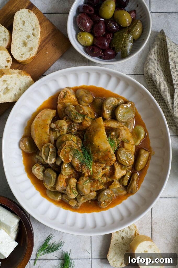 Greek artichokes with fava beans (Aginares me koukia) on a white plate surrounded by bread, olives and feta.
