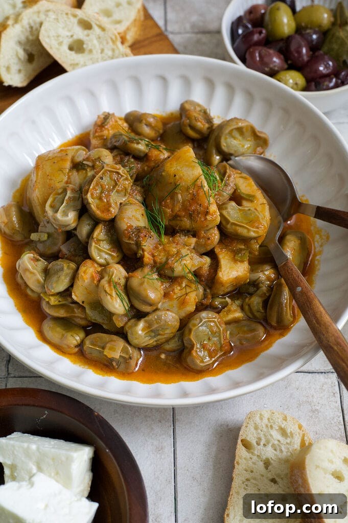 Greek artichokes with fava beans (Aginares me koukia) on a white plate surrounded by bread, olives and feta.