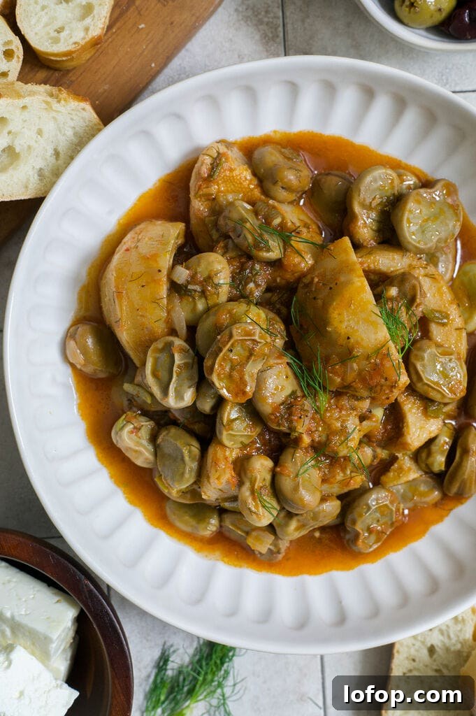 Greek artichokes with fava beans (Aginares me koukia) on a white plate surrounded by bread, olives and feta.