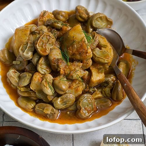Greek artichokes with fava beans (Aginares me koukia) on a white plate surrounded by bread, olives and feta.