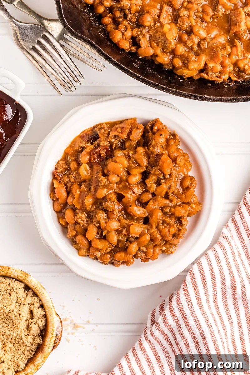 Hearty Baked Beans with Ground Beef — Stovetop, Oven or Slow Cooker 3 Overhead view of baked beans with ground beef in a white bowl.