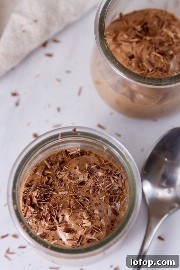 Creamy Cottage Cheese Chocolate Pudding Recipe 8 looking down at two small glass jars filled with chocolate pudding topped with chocolate shavings and a spoon next to them.
