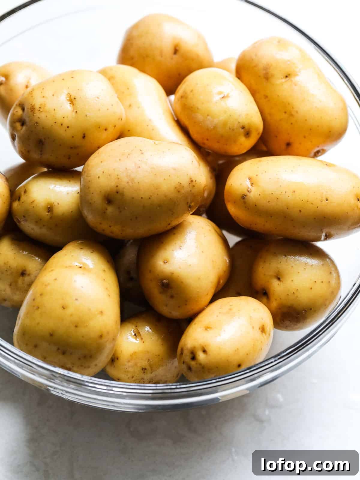 Crispy Oven-Roasted Potatoes with Garlic and Herbs 14 A large clear glass bowl filled with baby potatoes ready to use in a recipe.