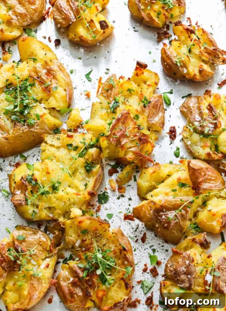 A sheet pan of smashed potatoes with fresh herbs baked with crispy golden brown edges.
