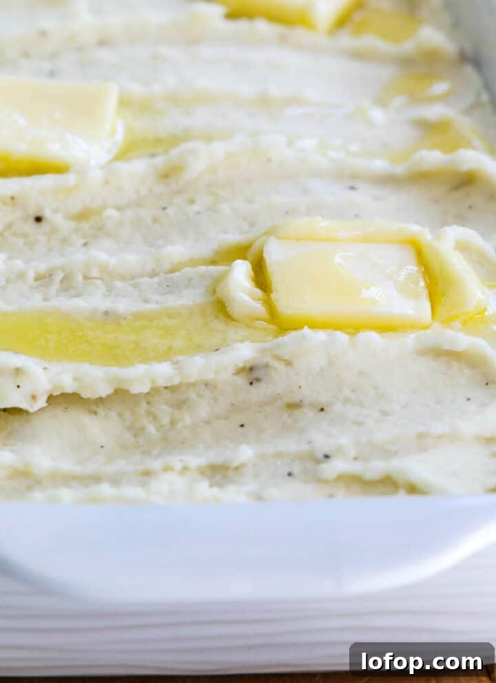 A white casserole dish filled with mashed potatoes and squares of melted butter on top.