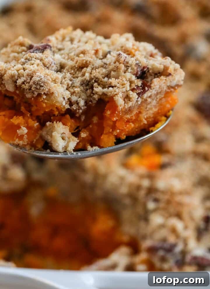 Lifting a scoop of sweet potato casserole out of a white casserole dish with large serving spoon.