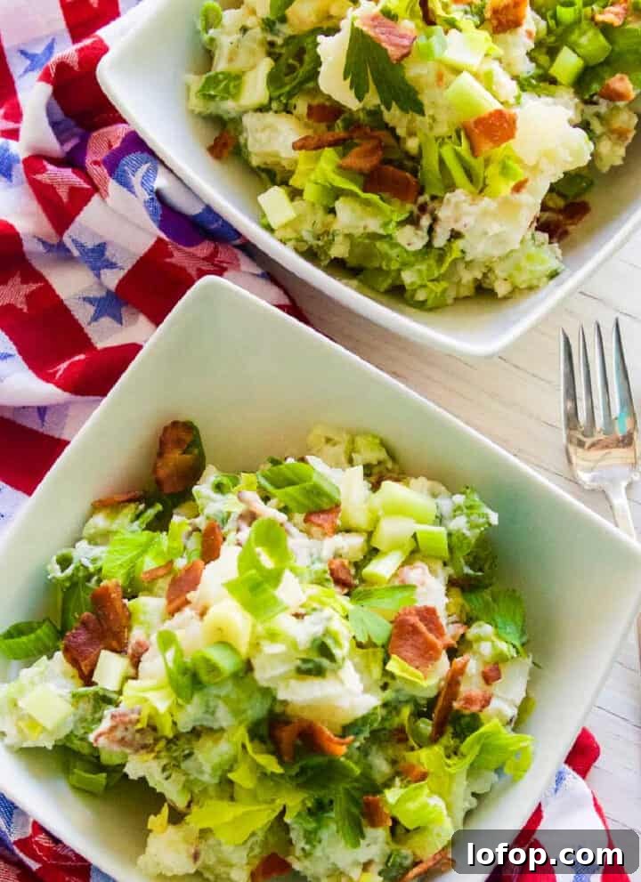 A small white bowl filled with bacon potato salad garnished with crispy bacon.