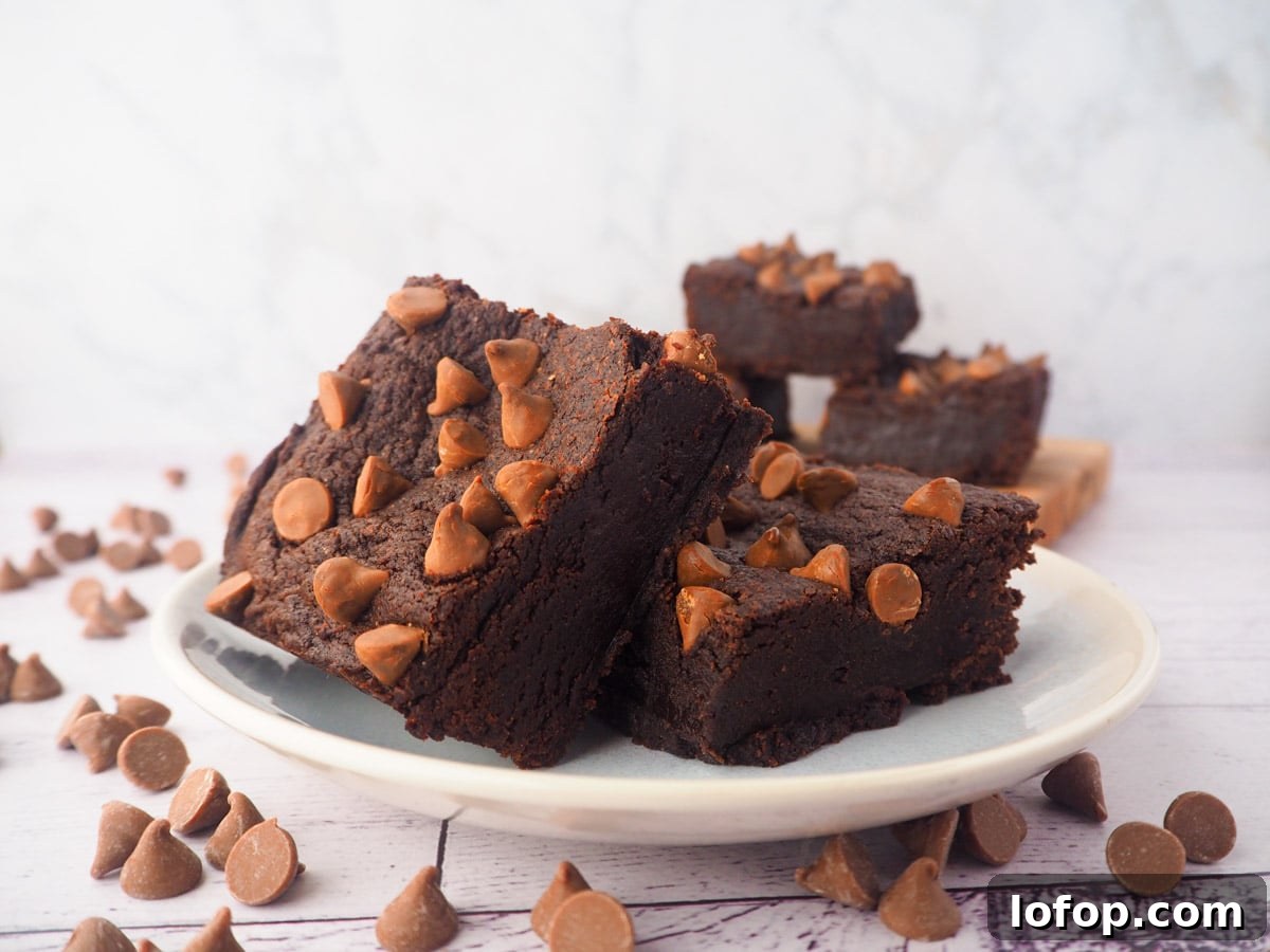Decadent Egg-Free Brownies Recipe for Fudgy Chocolate Bliss 15 Two eggless brownies on a plate, with a stack of eggless brownies in the background, and chocolate chips scattered around.