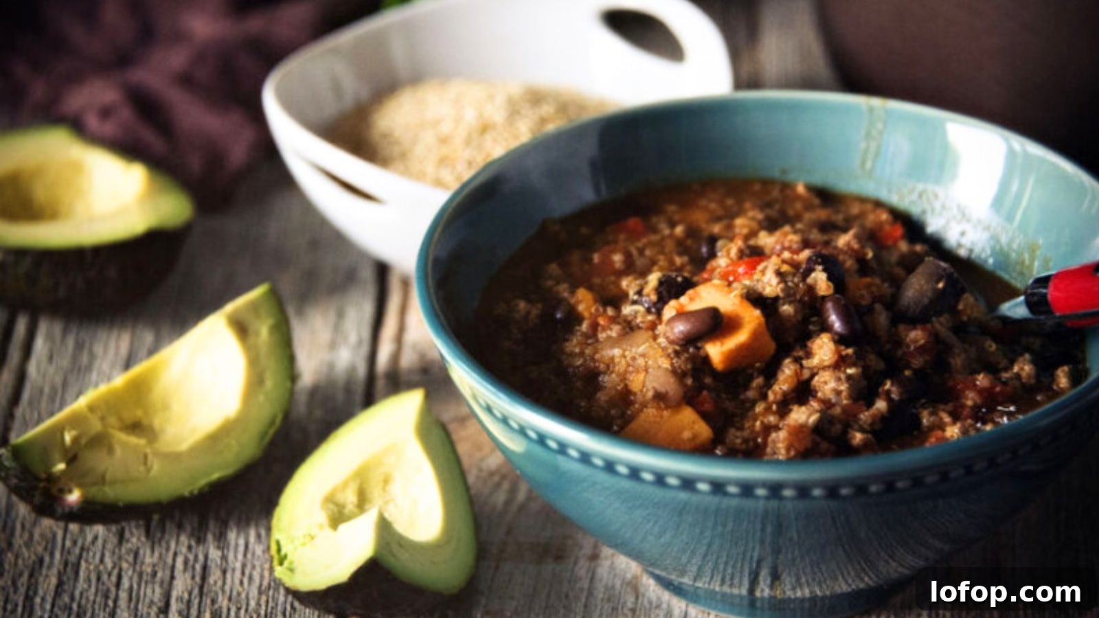 12 Epic Chili Recipes for Game Day Crowd-Pleasing Flavor 13 A delicious bowl of chili with beans, meat, and vegetables is on a table, embodying the essence of classic chili recipes. Next to it are creamy avocado slices and a bowl of wholesome grains, ready to be enjoyed.