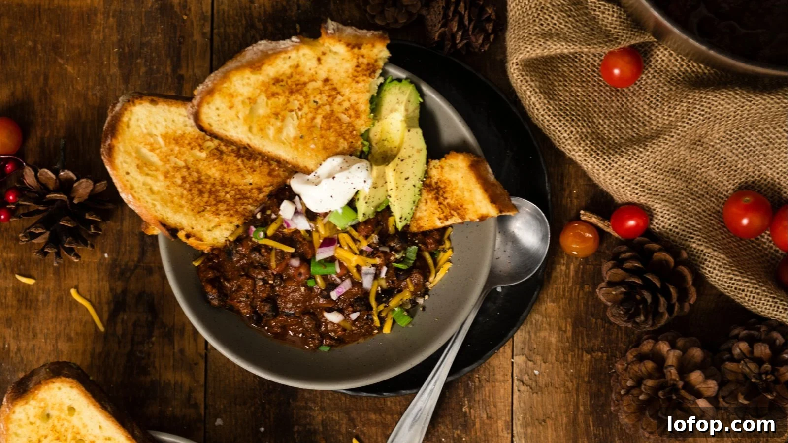 12 Epic Chili Recipes for Game Day Crowd-Pleasing Flavor 7 A bowl of chili topped with cheese, red onions, avocado, and sour cream, served with toasted bread.