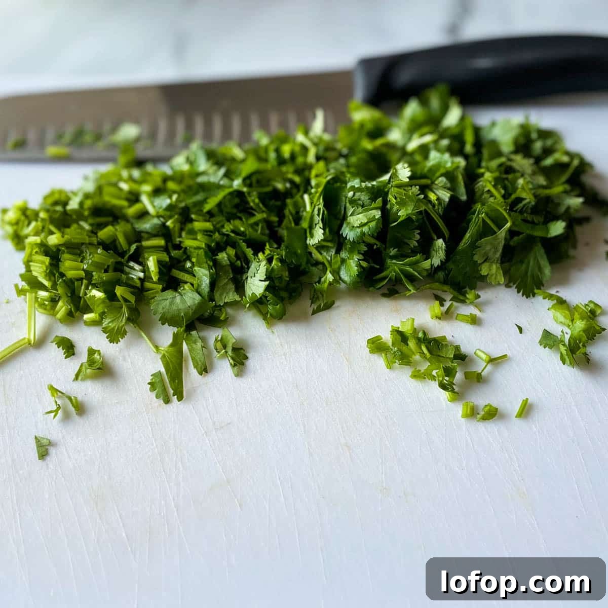 Tangy Pineapple Habanero Salsa Recipe for Grilling and Tacos 6 Chopped fresh cilantro is shown on a white cutting board with a kitchen knife in the background.