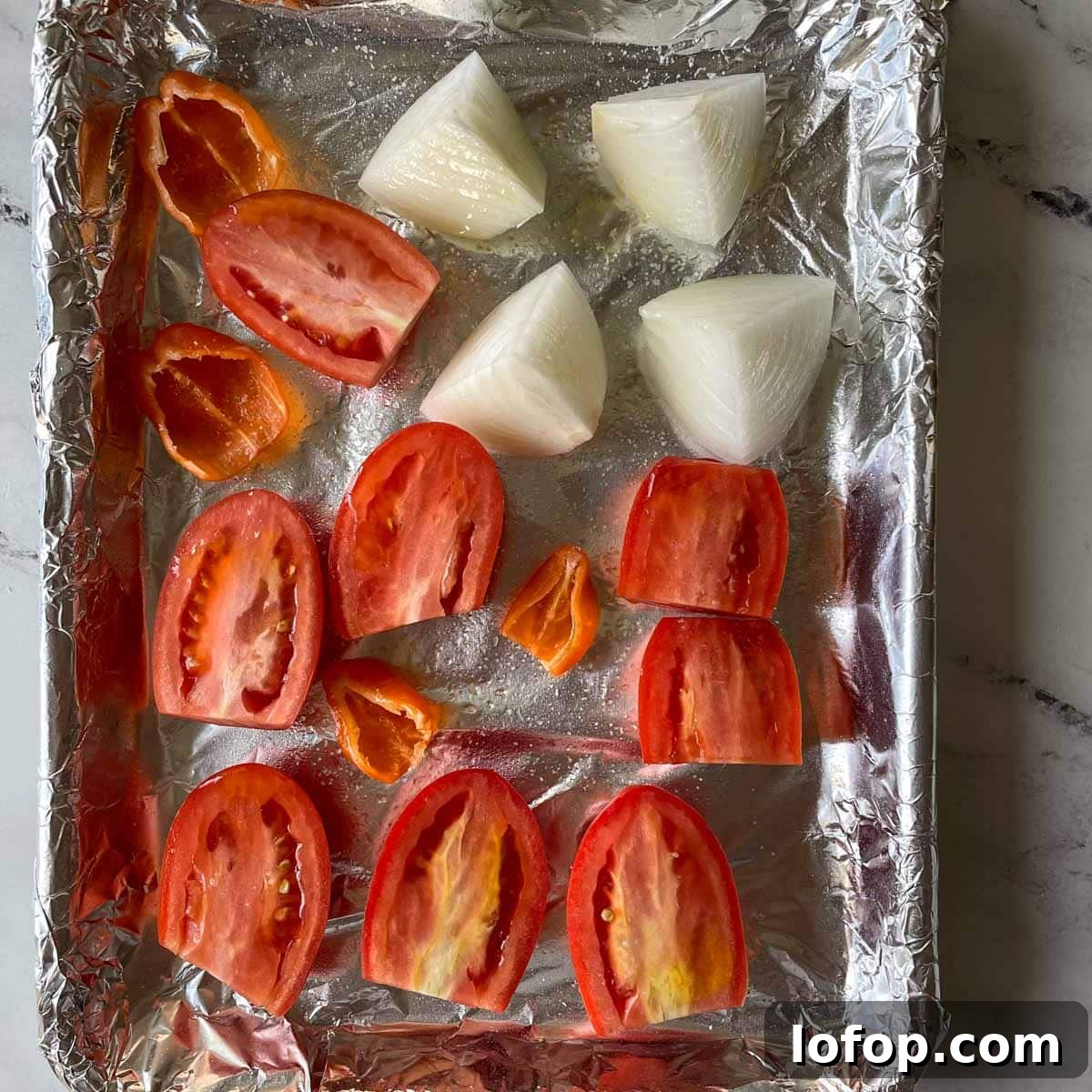 Tangy Pineapple Habanero Salsa Recipe for Grilling and Tacos 7 Halved tomatos and habaneros and half of a quartered white onion are shown a sheet tray covered with tin foil.