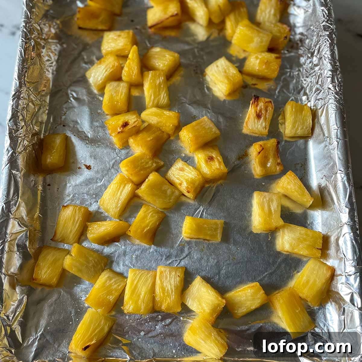 Tangy Pineapple Habanero Salsa Recipe for Grilling and Tacos 8 Roasted pieces of pineapple sit on a sheet tray lined with tin foil.