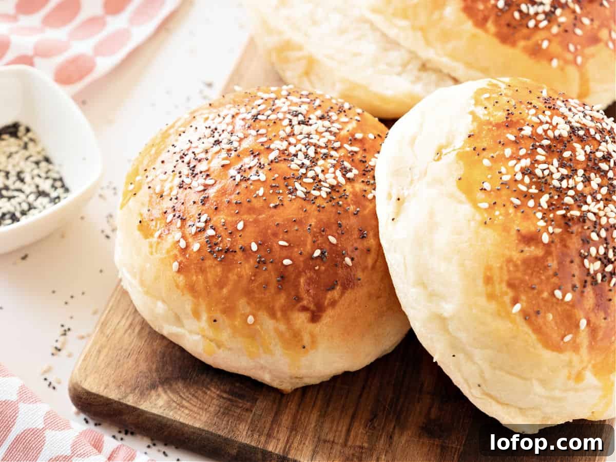 Perfectly Soft Homemade Burger Buns Recipe 3 Two hamburger buns with seeds on a wooden board.