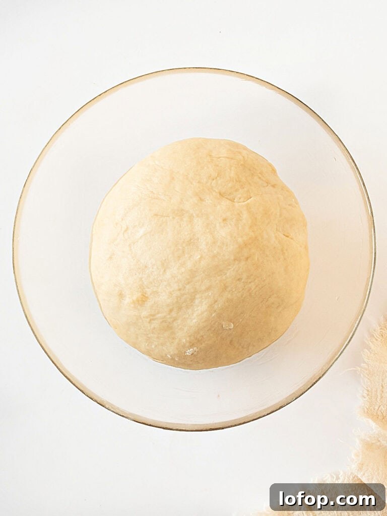 Perfectly Soft Homemade Burger Buns Recipe 6 Bread dough in a glass bowl. White background.