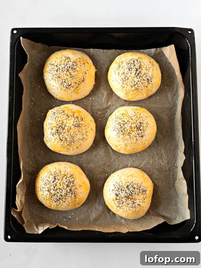 Perfectly Soft Homemade Burger Buns Recipe 9 Burger buns with seeds before baking on parchment paper. Black baking tray.
