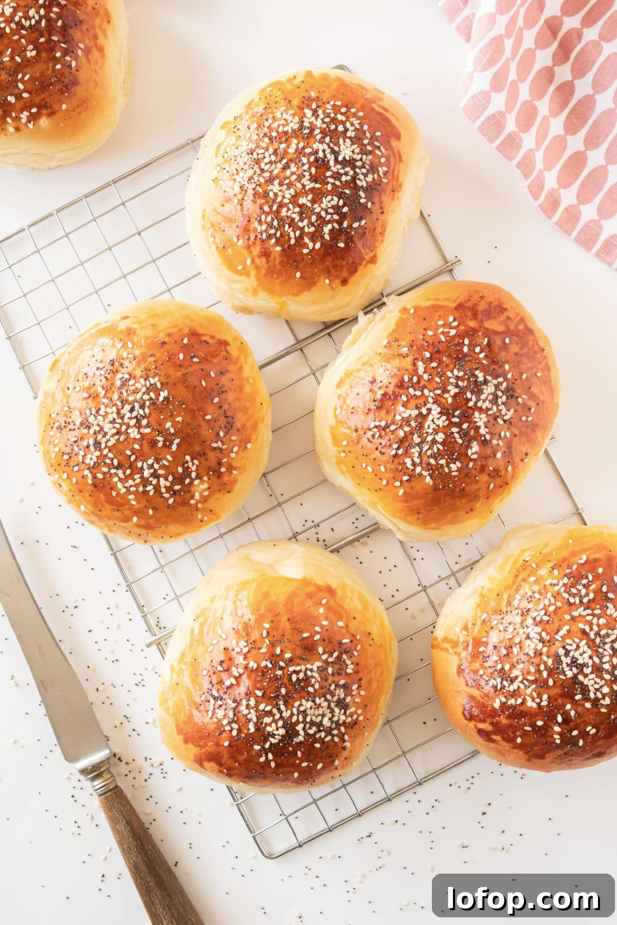 Perfectly Soft Homemade Burger Buns Recipe 10 Wire rack with sesame-topped hamburger buns. White background.