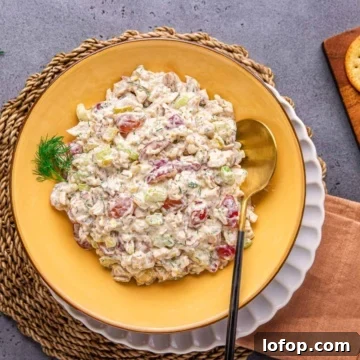 chicken salad with grapes in a yellow bowl with salad spoon and napkin on a flat surface.