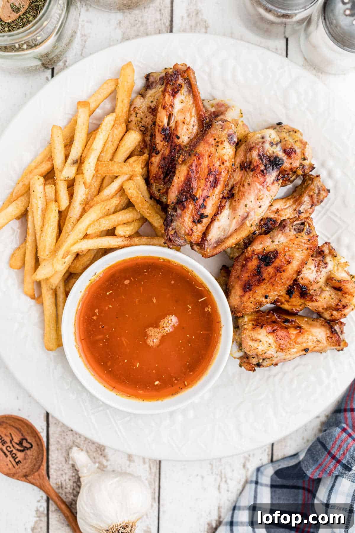 overhead shot of a plate of chicken wings, french fries and cajun butter sauce.
