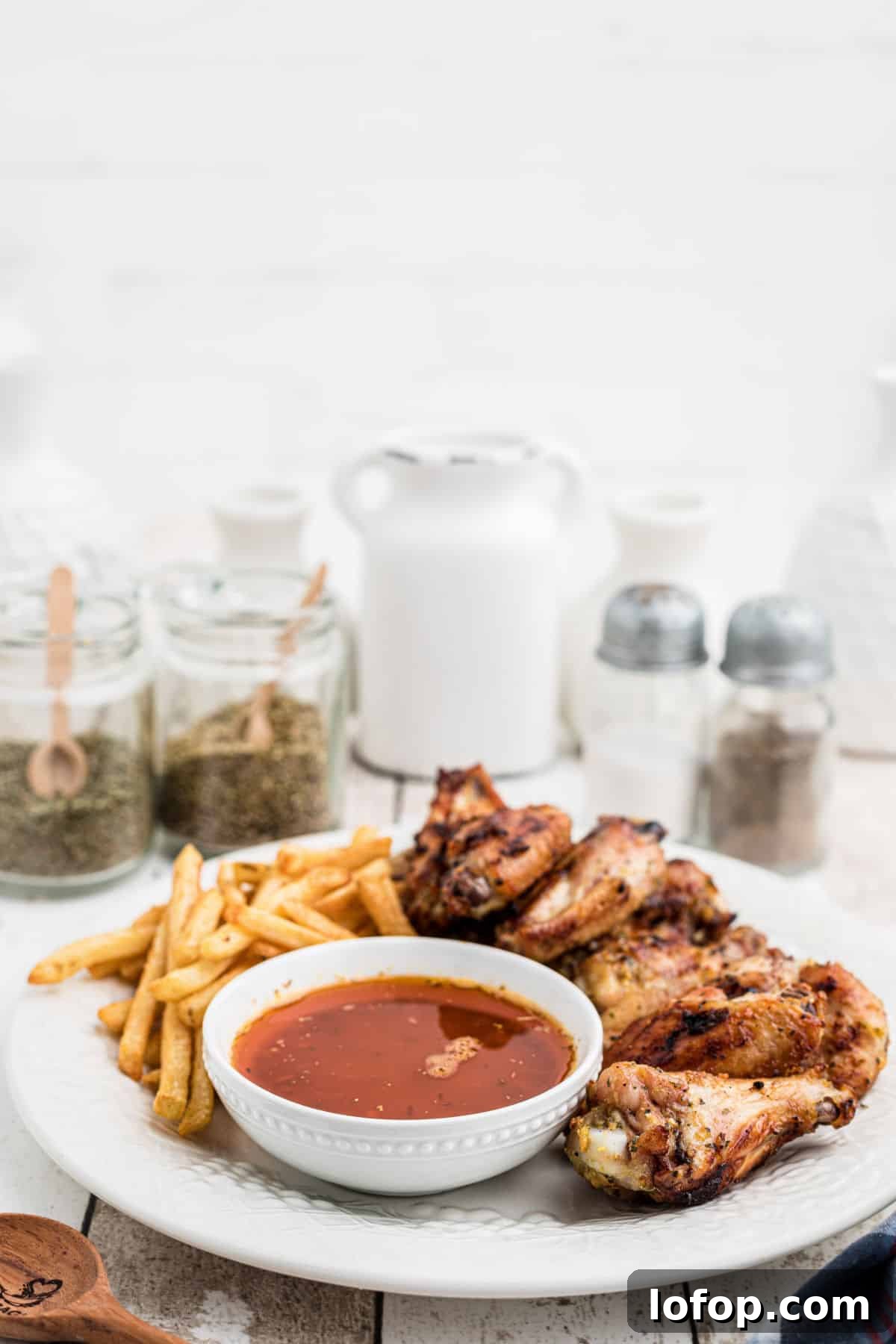 side view of a plate of chicken wings with french fries and cajun butter sauce.