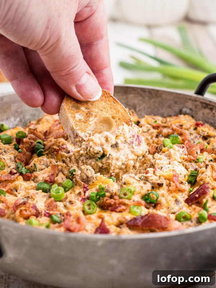 a skillet with some boudin dip cooked and some green onions sprinkled on top with a hand dipping into the dip