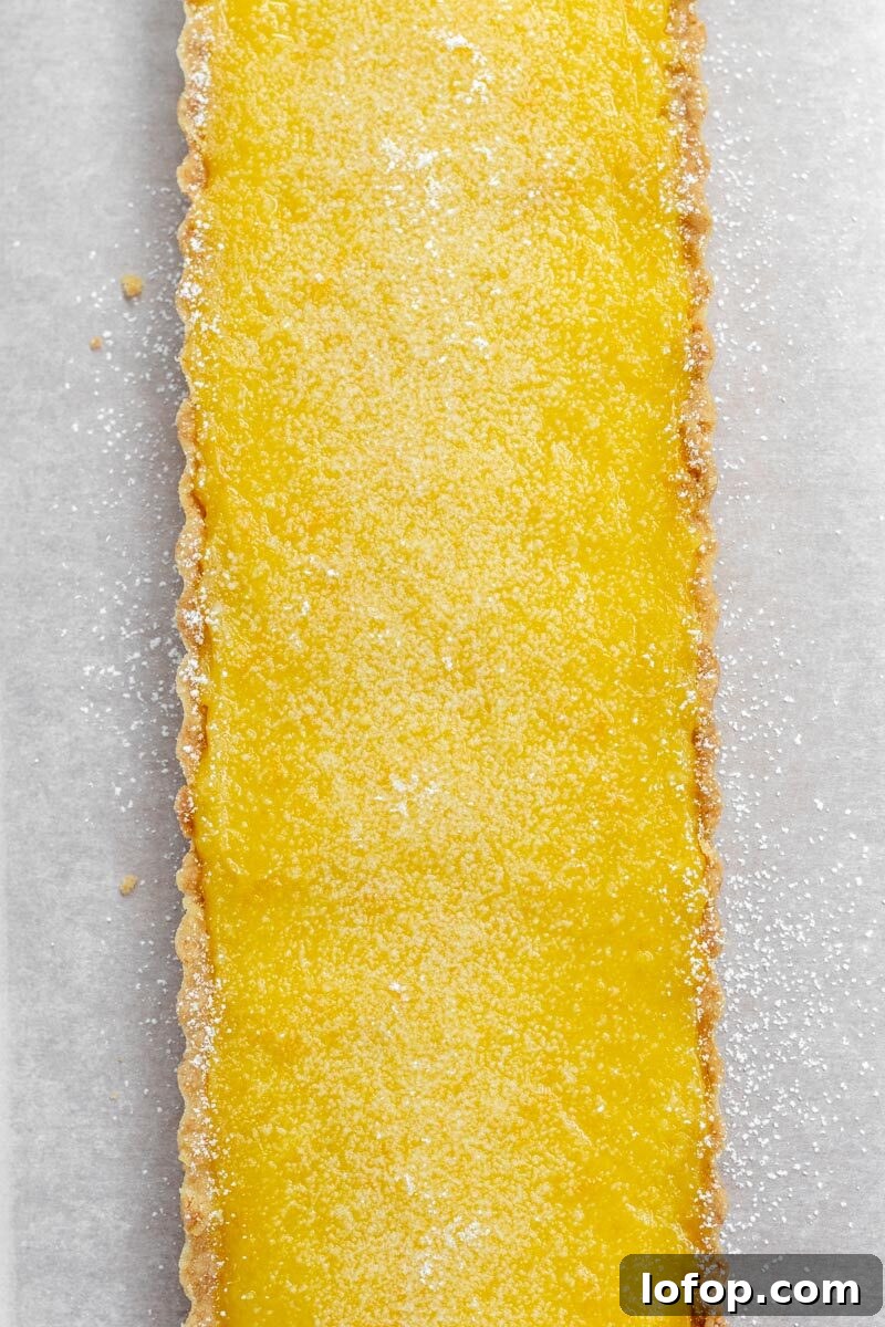 Meyer Lemon and Olive Oil Tart Recipe for Bright, Silky Dessert 3 A bright yellow rectangular lemon tart sprinkled with powdered sugar.