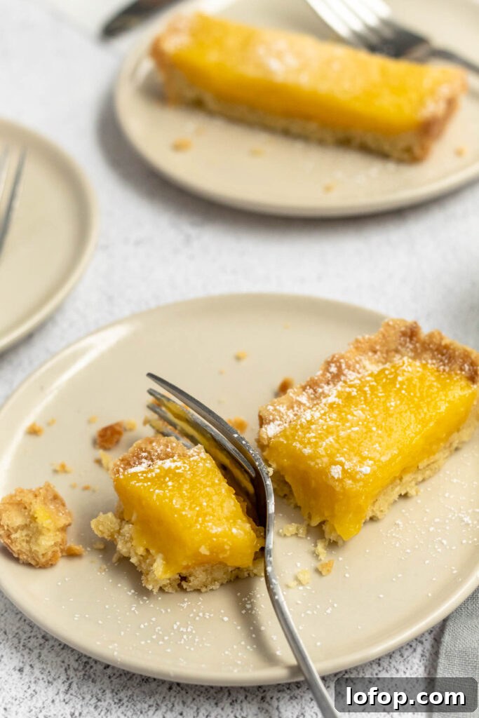 Meyer Lemon and Olive Oil Tart Recipe for Bright, Silky Dessert 7 A slice of bright yellow lemon tart on a plate with a fork.