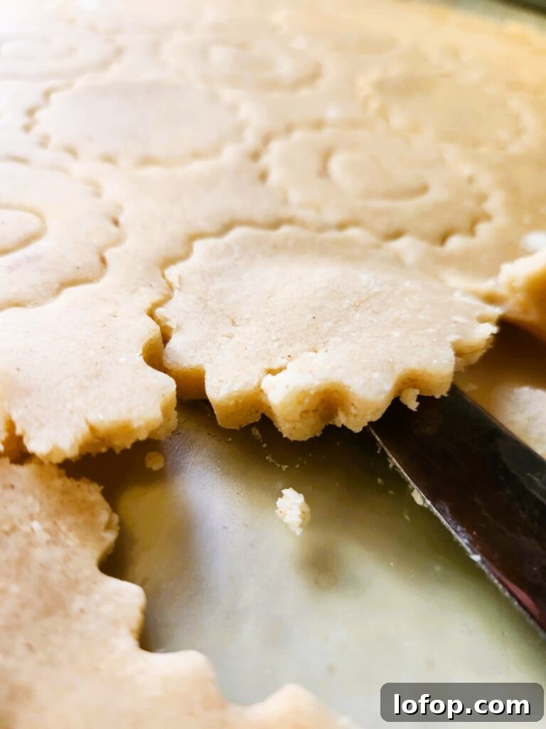Lifting cut-out cookies from the board using a butter knife.