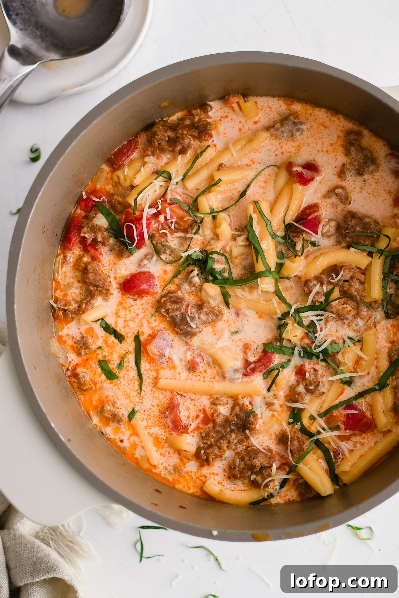 Large soup pot filled with cooked Italian sausage soup garnished with fresh basil.