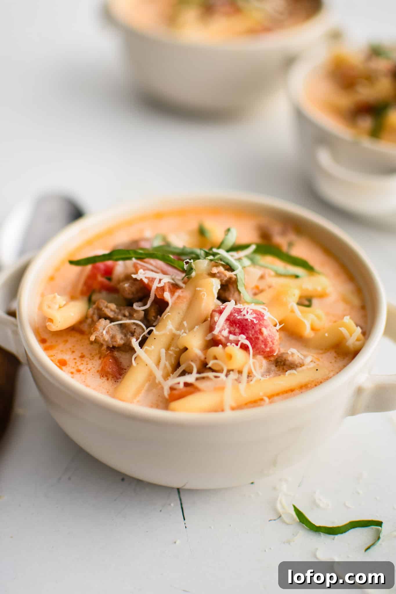 White soup bowl filled with creamy tomato-based Italian Sausage Soup garnished with fresh basil and parmesan cheese.