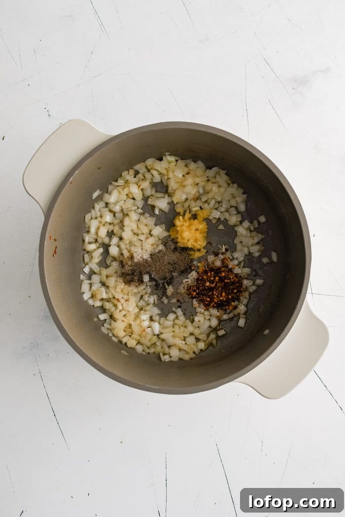 Minced garlic, red pepper, salt, and pepper added to softened white onion cooking in a large soup pot.
