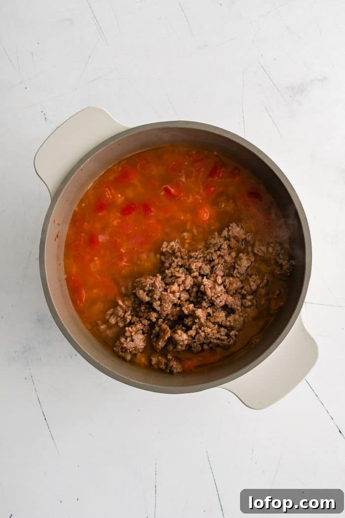 Cooked ground Italian sausage added back to a large soup filled with diced tomatoes, chicken broth, and onions.