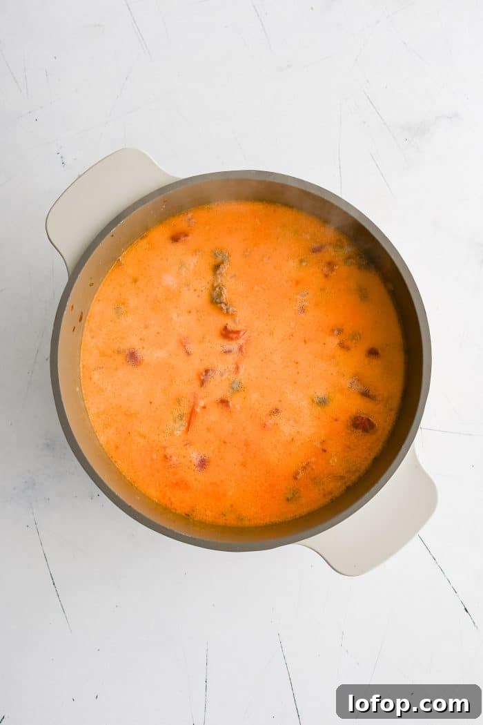 Heavy cream added to a large soup pot containing cooked pasta, ground Italian sausage, diced tomatoes, chicken broth, onions, and spices.